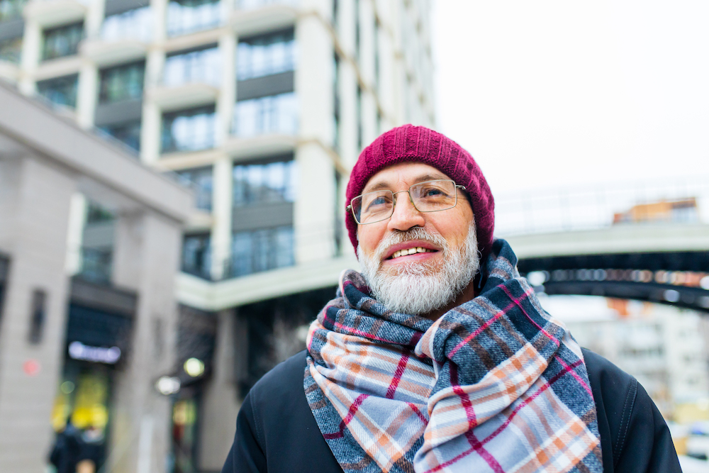 An older man dressed in winter wear smiling while walking through a city