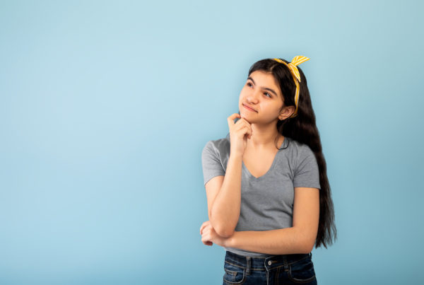 Thinking Indian teen girl looking upwards at copy space, posing on blue studio background.