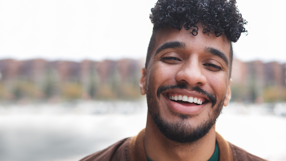 Happy Latin man portrait smiling and looking at camera outdoor with city in background