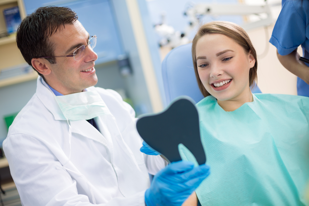Orthodontist showing female patient her smile in dental mirror during orthodontic consultation for confidence improvement